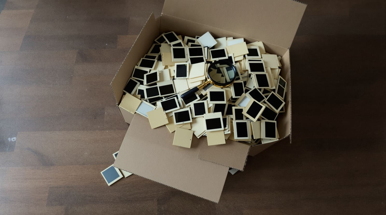 A cardboard box of loose yellowed 35mm slides on a kitchen table, seen from above
