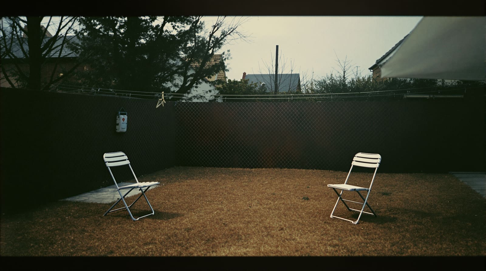 A faded seventies snapshot of an empty back garden with two folding chairs