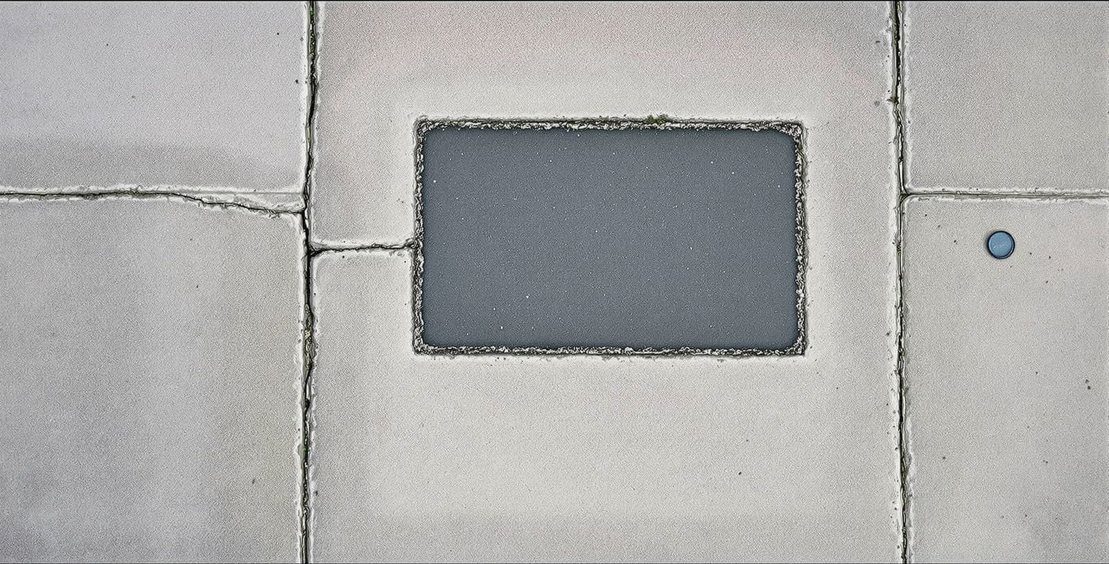 Cracked and patched concrete sidewalk seen from directly above in flat grey daylight